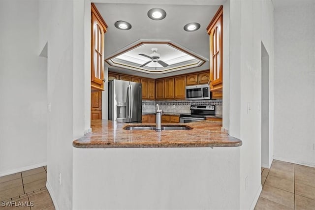 kitchen with a raised ceiling, sink, light tile patterned floors, light stone counters, and stainless steel appliances