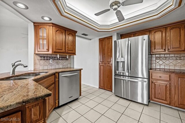 kitchen with sink, dark stone counters, ornamental molding, a raised ceiling, and stainless steel appliances