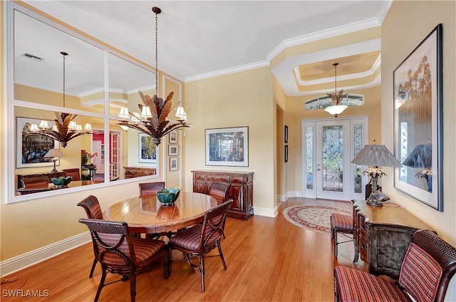 dining room with a tray ceiling, visible vents, an inviting chandelier, ornamental molding, and wood finished floors