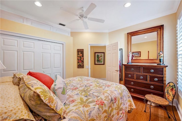 bedroom featuring ceiling fan, wood finished floors, visible vents, a closet, and crown molding