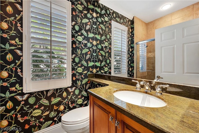 bathroom with toilet, wallpapered walls, a shower with shower door, and vanity