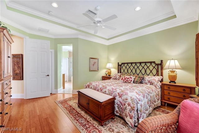 bedroom with light wood-style flooring, visible vents, baseboards, a raised ceiling, and crown molding