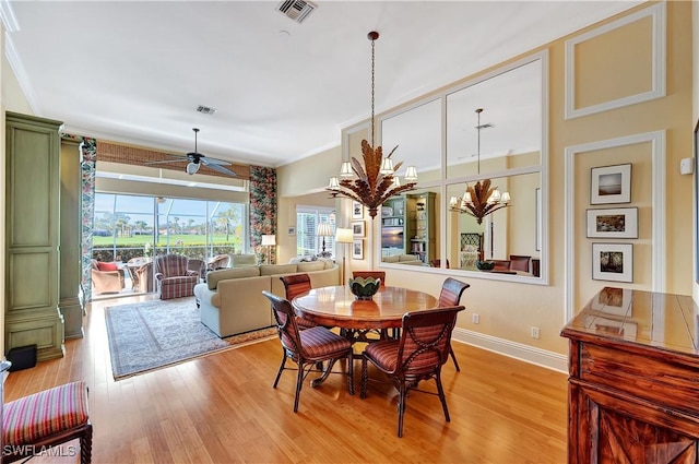 dining space with ceiling fan with notable chandelier, visible vents, baseboards, light wood-type flooring, and crown molding