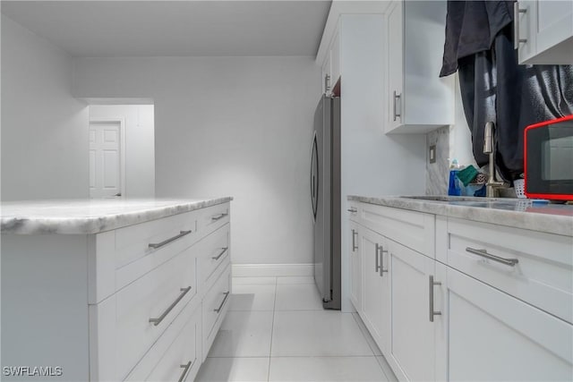 kitchen with stainless steel refrigerator, sink, light tile patterned floors, and white cabinets