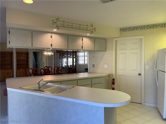 kitchen featuring sink, white refrigerator, light tile patterned floors, kitchen peninsula, and an inviting chandelier