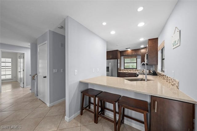 kitchen with stainless steel fridge with ice dispenser, sink, a kitchen breakfast bar, decorative backsplash, and kitchen peninsula