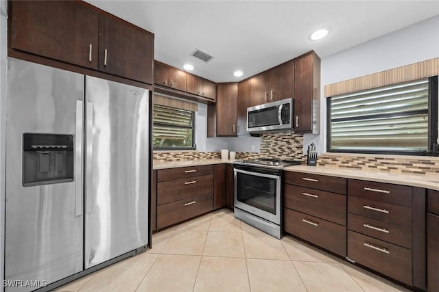 kitchen featuring dark brown cabinetry, appliances with stainless steel finishes, decorative backsplash, and light tile patterned floors