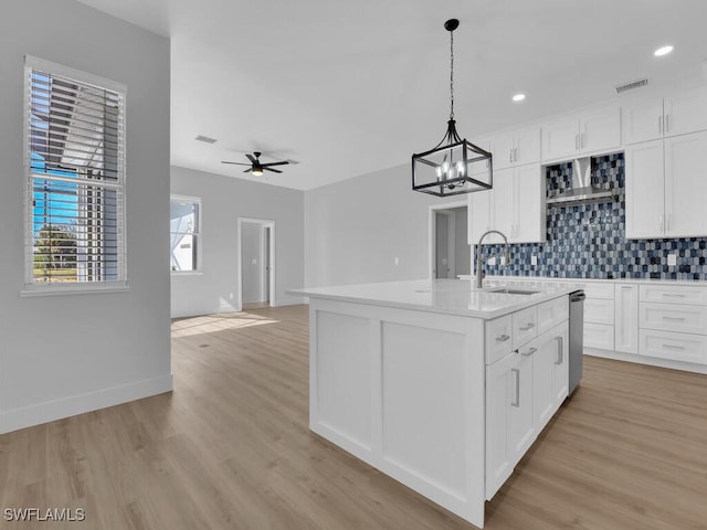 kitchen with sink, hanging light fixtures, a center island with sink, white cabinets, and backsplash