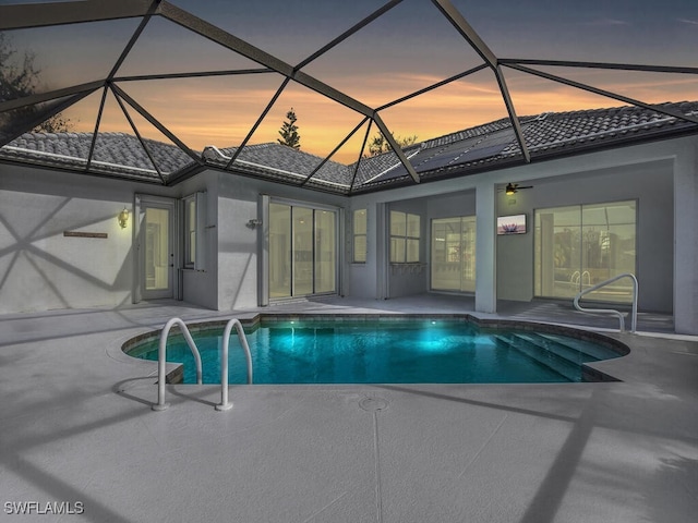 pool at dusk with a patio area and glass enclosure