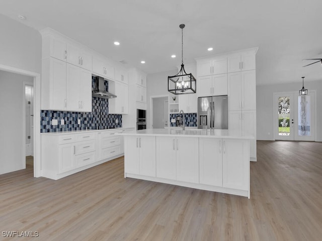 kitchen featuring wall chimney exhaust hood, appliances with stainless steel finishes, an island with sink, and white cabinets