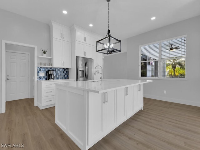 kitchen featuring decorative light fixtures, tasteful backsplash, white cabinetry, an island with sink, and stainless steel refrigerator with ice dispenser