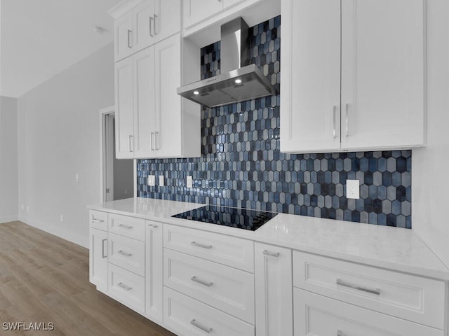 kitchen with wall chimney exhaust hood, white cabinetry, light hardwood / wood-style flooring, black electric cooktop, and light stone countertops