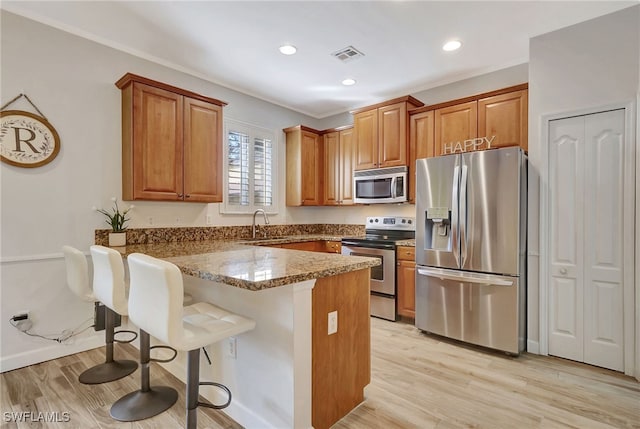 kitchen with dark stone countertops, a kitchen bar, light wood-type flooring, and appliances with stainless steel finishes