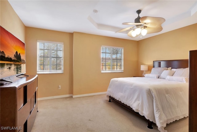 bedroom featuring ceiling fan, a tray ceiling, light carpet, and multiple windows