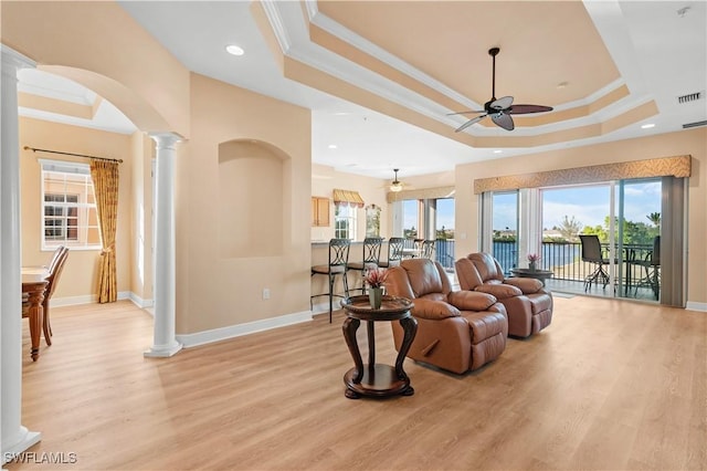 living room with ceiling fan, ornamental molding, light hardwood / wood-style floors, a raised ceiling, and ornate columns