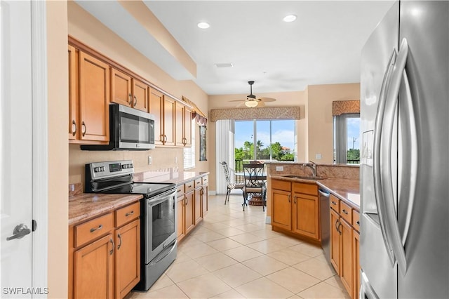 kitchen featuring sink, light stone counters, light tile patterned floors, appliances with stainless steel finishes, and ceiling fan