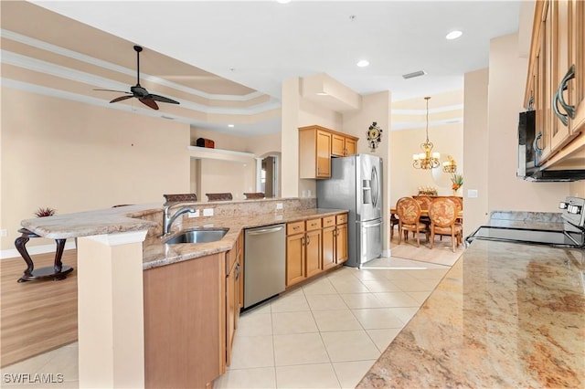 kitchen with sink, appliances with stainless steel finishes, a kitchen breakfast bar, a tray ceiling, and light stone countertops