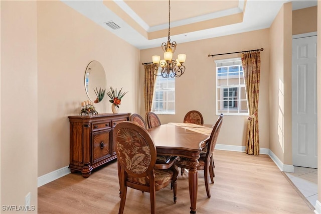 dining area featuring a notable chandelier, crown molding, a raised ceiling, and light wood-type flooring