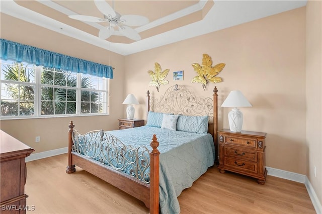 bedroom featuring light hardwood / wood-style flooring, ceiling fan, and a tray ceiling