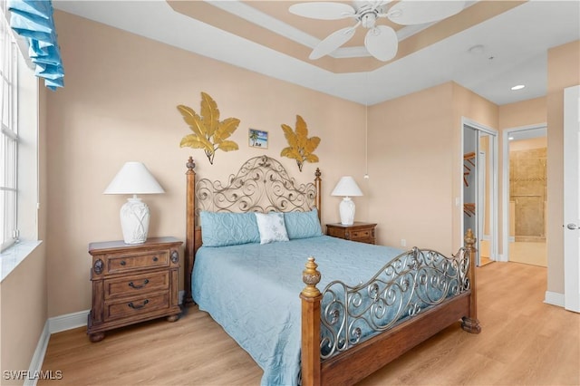 bedroom with ceiling fan, a tray ceiling, light hardwood / wood-style floors, and a closet