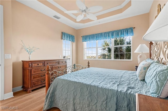 bedroom with ceiling fan, ornamental molding, a tray ceiling, and light hardwood / wood-style flooring