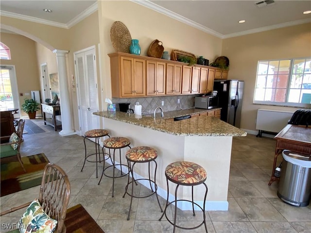 kitchen with a wealth of natural light, decorative columns, sink, backsplash, and black fridge with ice dispenser