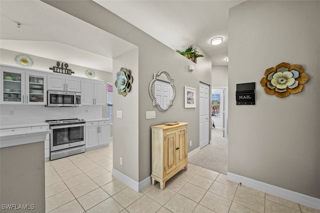 kitchen with stainless steel appliances, lofted ceiling, light tile patterned floors, and white cabinets