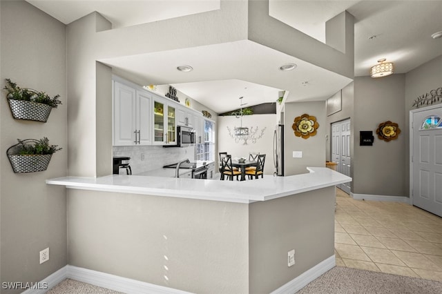 kitchen featuring white cabinetry, light tile patterned floors, kitchen peninsula, stainless steel appliances, and decorative backsplash