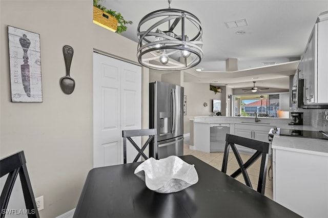 tiled dining area featuring sink and ceiling fan with notable chandelier