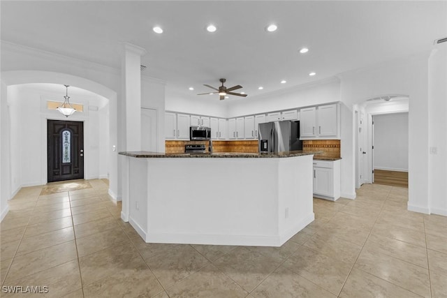 kitchen with arched walkways, white cabinets, decorative backsplash, dark stone counters, and appliances with stainless steel finishes