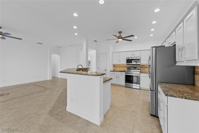 kitchen with white cabinetry, decorative backsplash, dark stone counters, ceiling fan, and stainless steel appliances