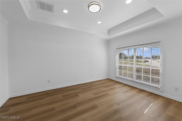 empty room with hardwood / wood-style flooring, ornamental molding, and a tray ceiling