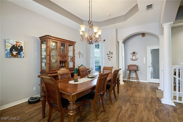 dining area featuring dark hardwood / wood-style flooring, a notable chandelier, a tray ceiling, and ornate columns