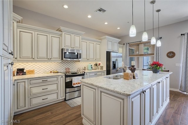 kitchen featuring appliances with stainless steel finishes, pendant lighting, dark hardwood / wood-style flooring, light stone counters, and a center island with sink