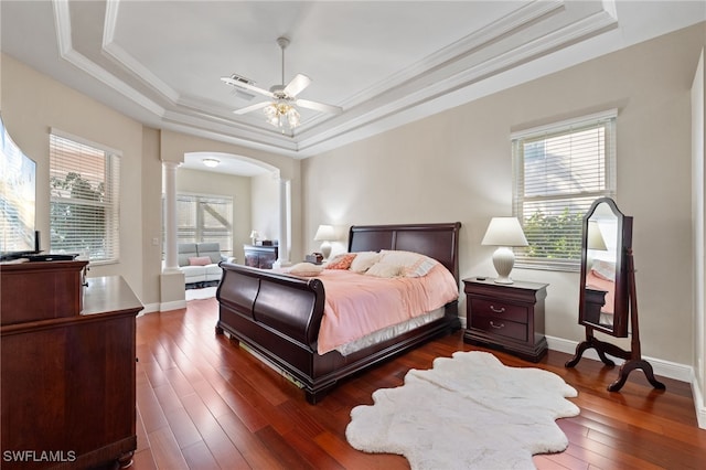 bedroom featuring arched walkways, crown molding, dark wood finished floors, decorative columns, and a raised ceiling