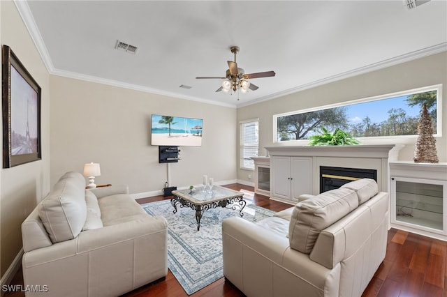 living room featuring dark wood-style flooring, visible vents, baseboards, ornamental molding, and a glass covered fireplace