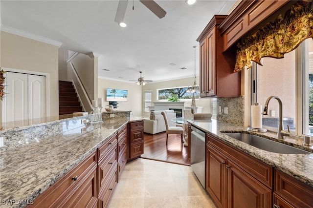 kitchen featuring hanging light fixtures, light stone countertops, a sink, crown molding, and stainless steel dishwasher