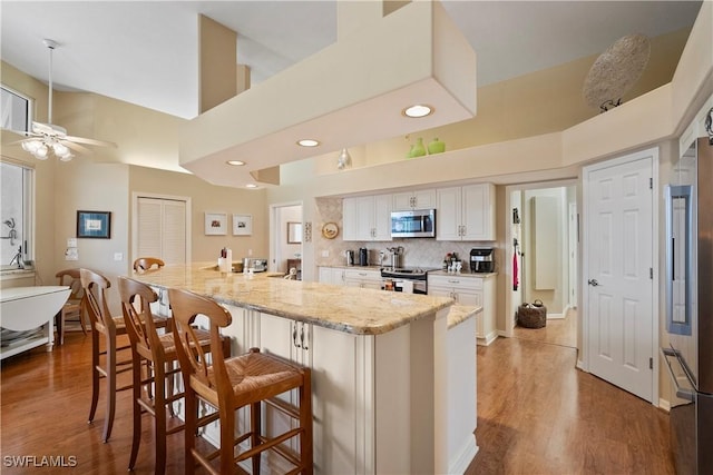 kitchen with a breakfast bar area, white cabinets, appliances with stainless steel finishes, backsplash, and light stone countertops