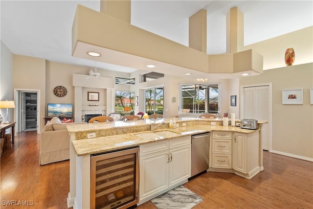 kitchen with beverage cooler, light stone counters, open floor plan, stainless steel dishwasher, and a sink