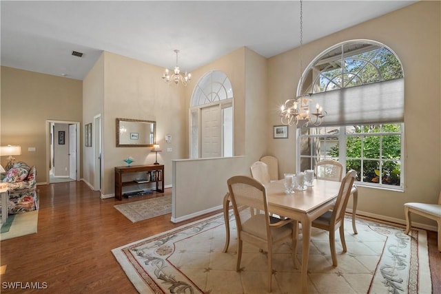 dining room with a notable chandelier, a towering ceiling, baseboards, and wood finished floors