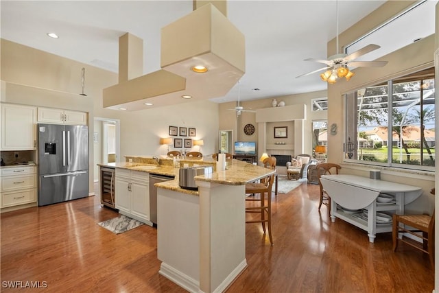 kitchen featuring beverage cooler, light stone counters, open floor plan, stainless steel appliances, and a large island with sink