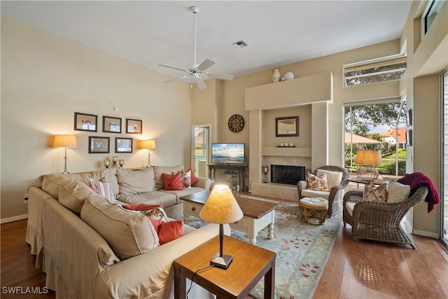 living room with baseboards, visible vents, a tiled fireplace, wood finished floors, and a high ceiling