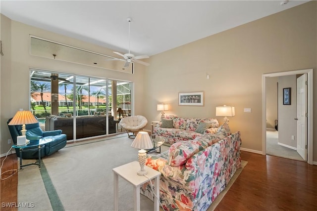 living room with ceiling fan, wood finished floors, a towering ceiling, and baseboards