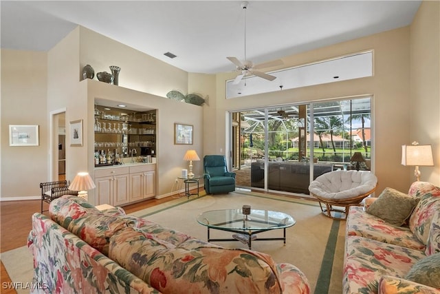 living area featuring a dry bar, ceiling fan, a high ceiling, and baseboards