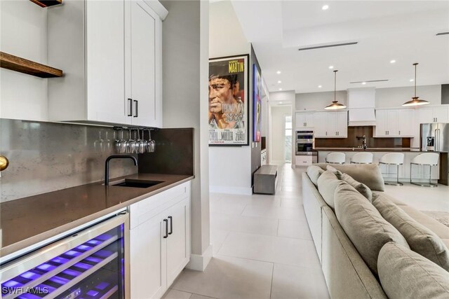 interior space with decorative light fixtures, white cabinetry, sink, beverage cooler, and stainless steel appliances