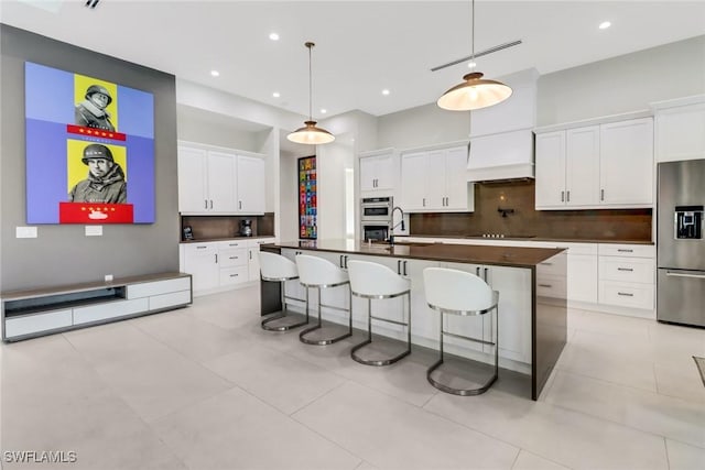 kitchen with appliances with stainless steel finishes, a breakfast bar area, an island with sink, decorative light fixtures, and white cabinetry