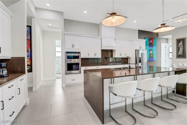 kitchen featuring an island with sink, sink, custom range hood, appliances with stainless steel finishes, and white cabinets