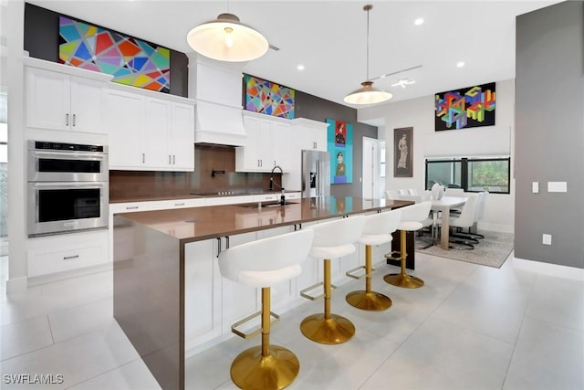 kitchen with appliances with stainless steel finishes, sink, a kitchen breakfast bar, decorative light fixtures, and white cabinets