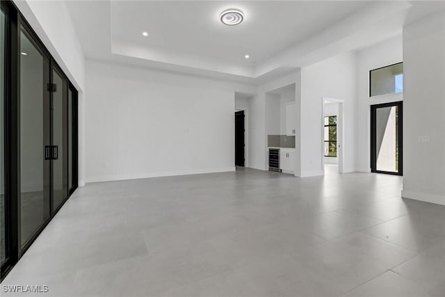 unfurnished living room with a raised ceiling, beverage cooler, and a high ceiling