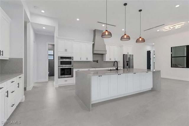 kitchen with hanging light fixtures, a spacious island, premium range hood, appliances with stainless steel finishes, and white cabinets